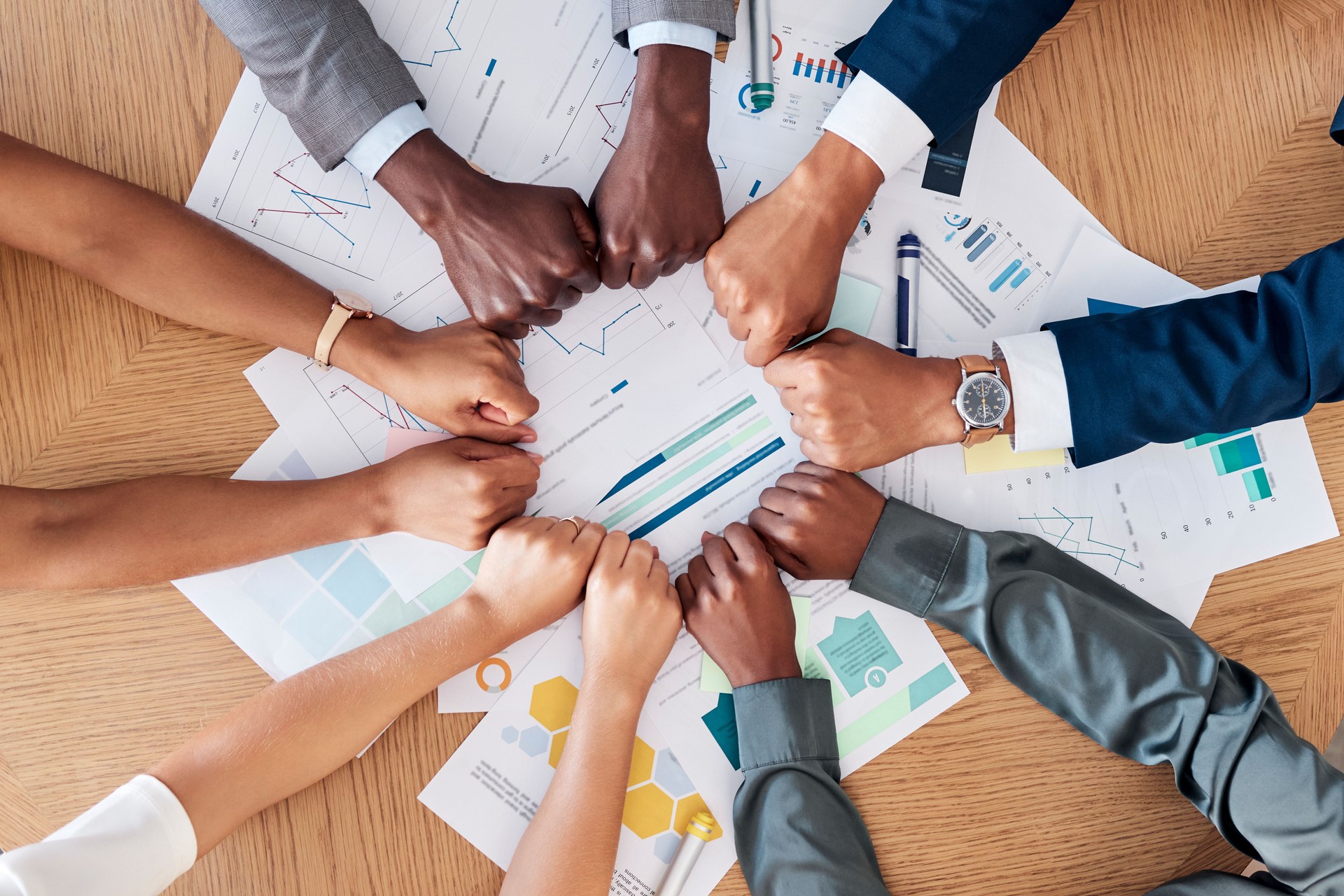 Teamwork, documents and circle of hands in fist in business meeting for strategy, planning and analytics. Collaboration, diversity and business people with paperwork, infographics and graphs on desk